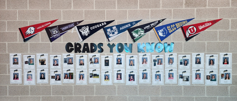 Wall display at Bountiful Elementary featuring the phrase “Grads You Know” in large letters, with college pennants across the top and staff graduation photos arranged in rows below on a brick wall.