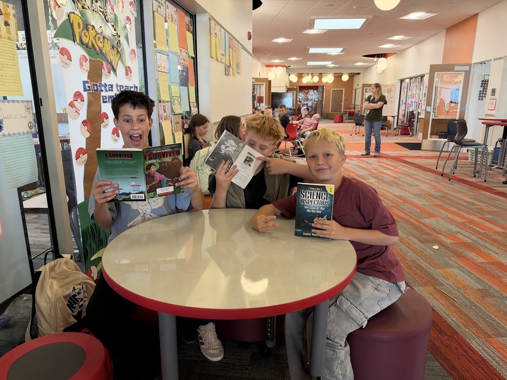 3 students posing for the camera reading their books.