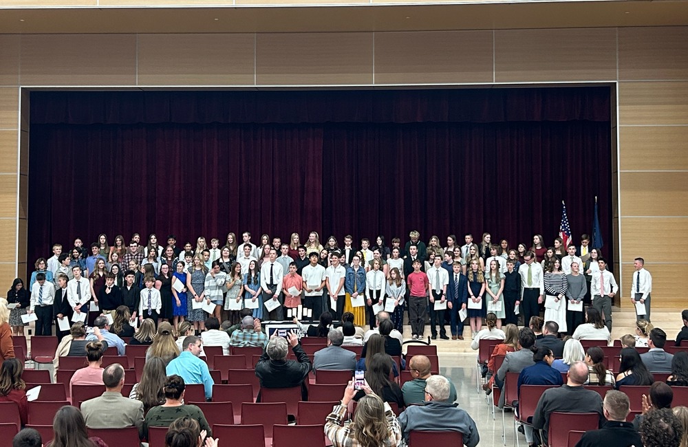 Students standing on a stage with families in the audience.