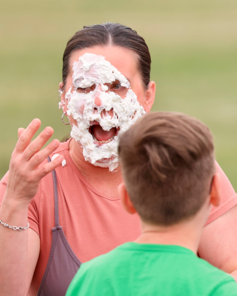 A teacher looks surprised after she has a pie shoved in her face.