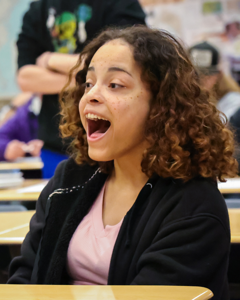 A student sitting at her desk opens her mouth in surprise. 