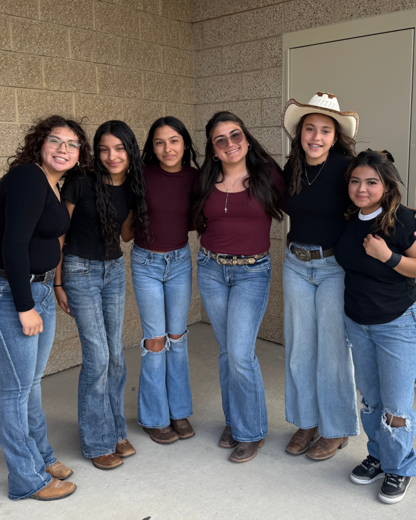 A group of students smiling at the camera. All of them are wearing either black or red shirts, jeans and boots.