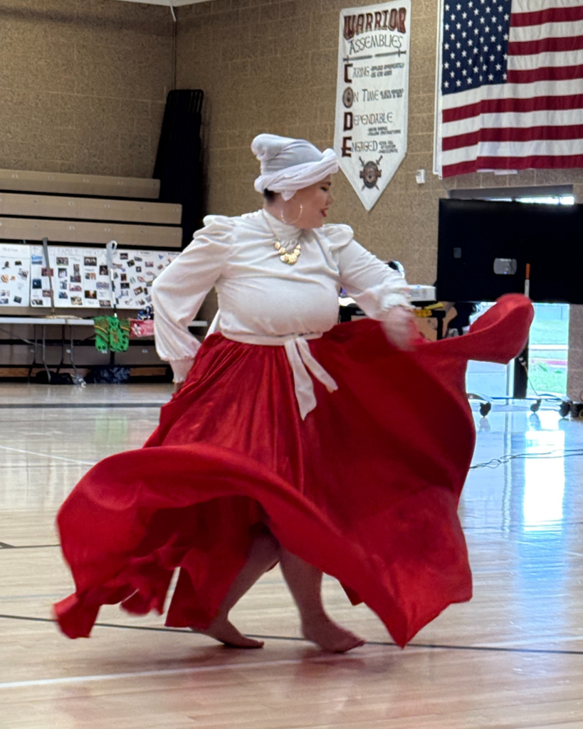 A student dancing in a red skirt whips their skirt around to create waves.