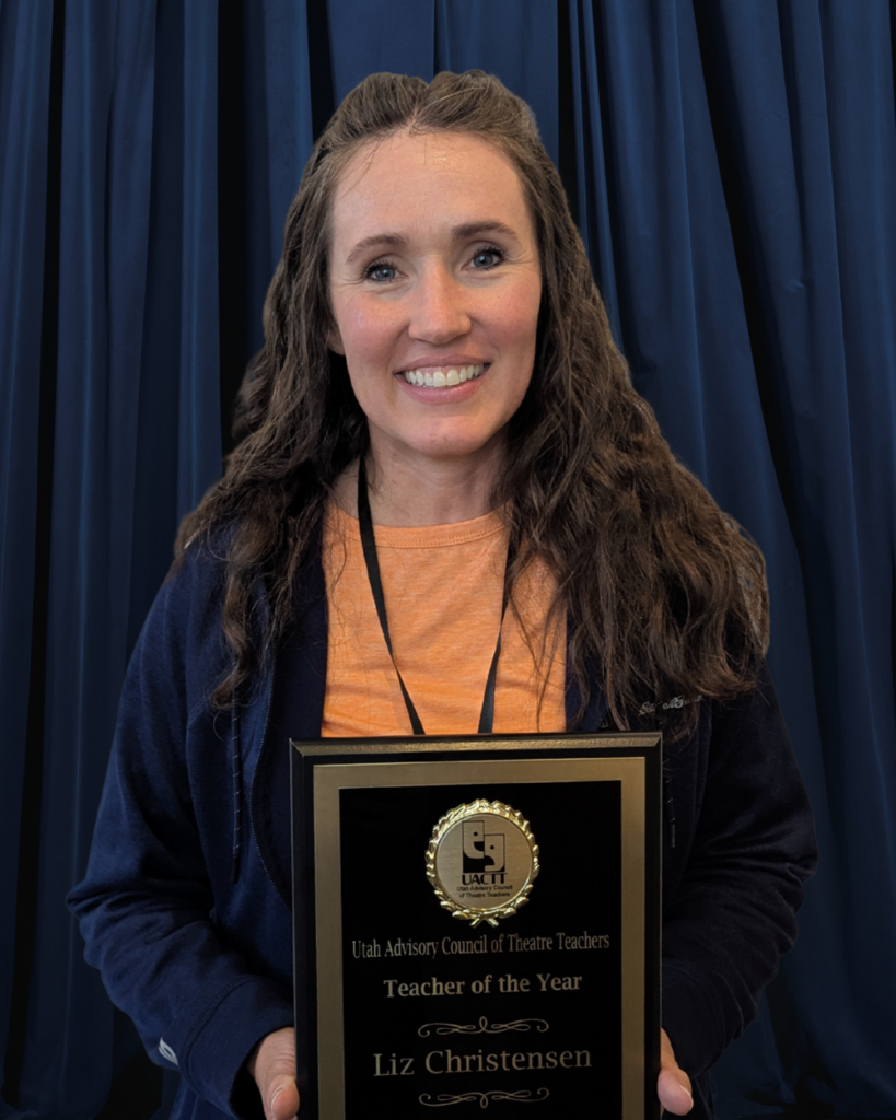 A photo of a female teacher with brown hair holding a plaque that says "UACTT Utah Advisory Council of Theatre Teachers Teacher of the Year Liz Christensen.