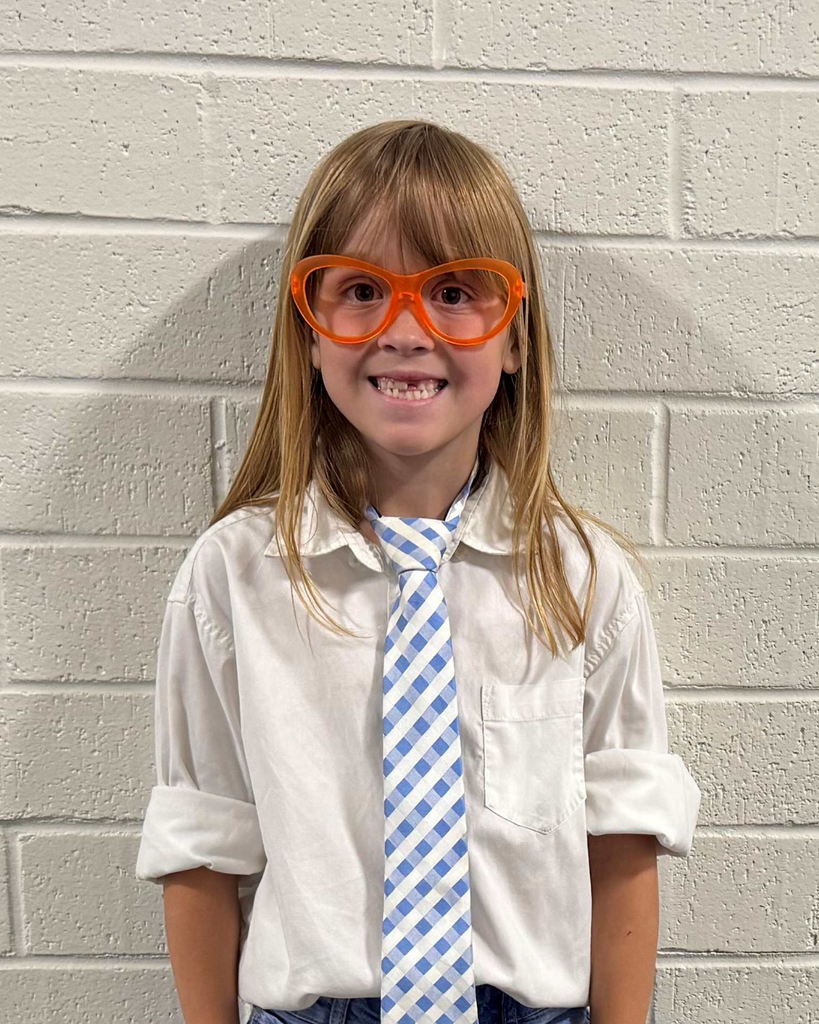 A girl smiles at the camera while wearing a white button down shirt, a tie and orange glasses.