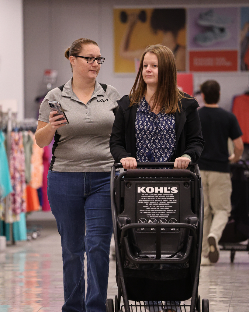 Two people pushing one Kohl's cart walking down the hall.
