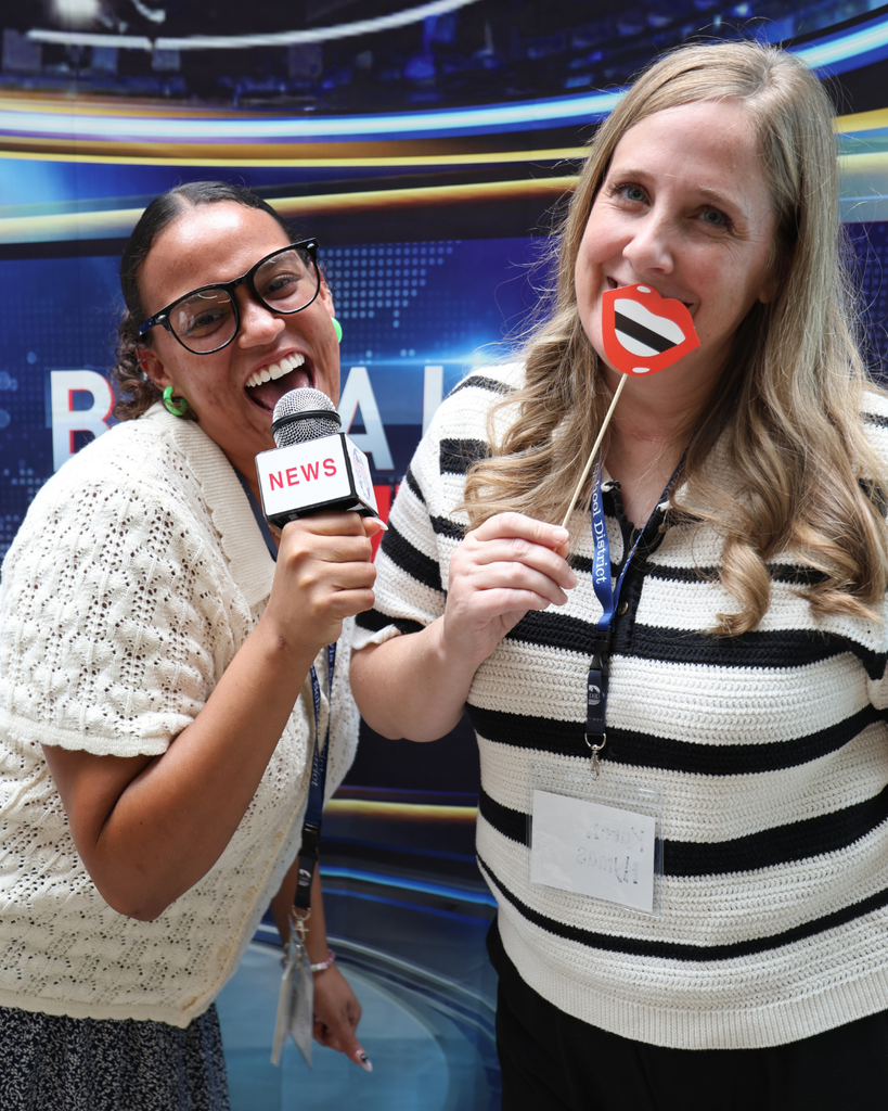 Two new educators smiling and having fun. One is holding a news anchor mic and the other is holding red smiling lips.