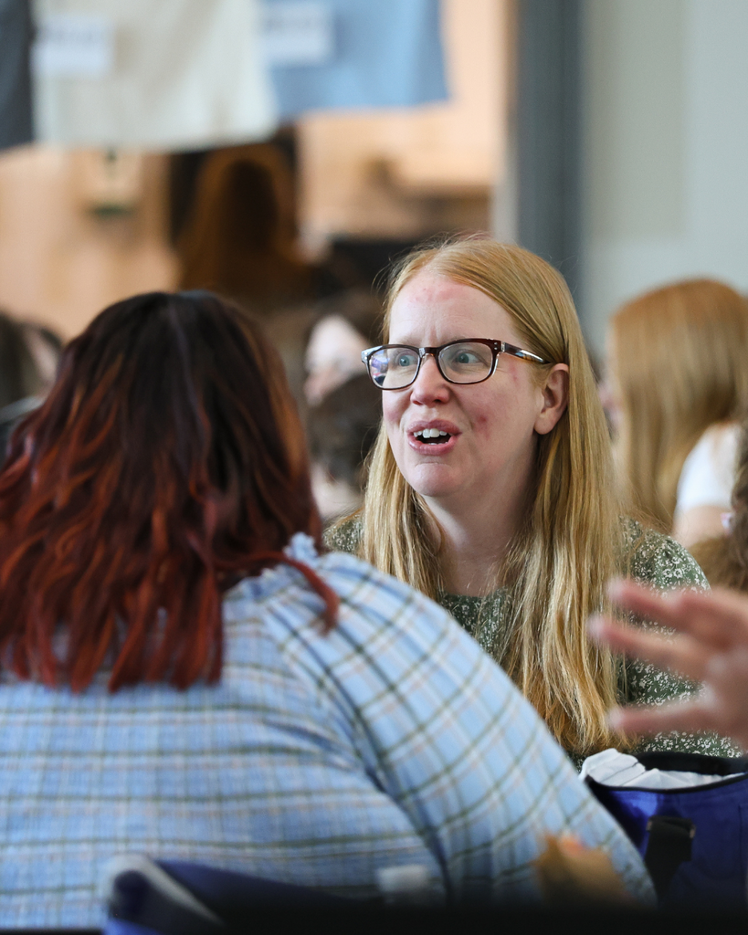 A crowd of new educators eating lunch. One is particularly engaged in a conversation.