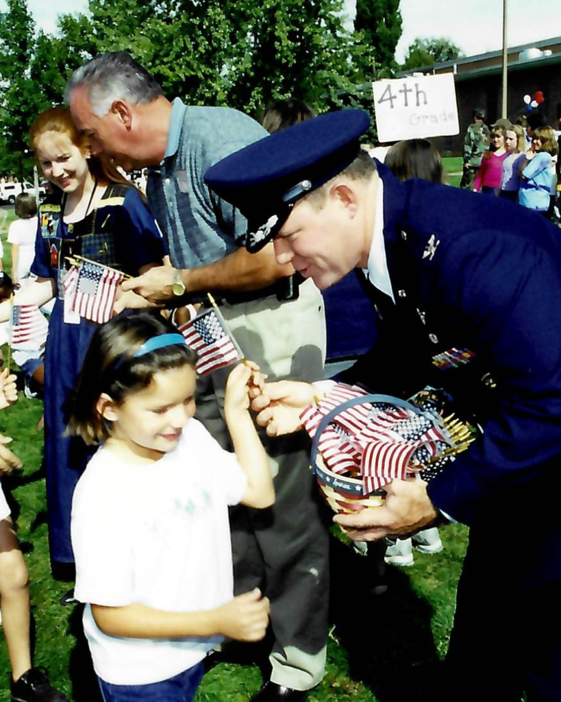 A military person handing out flags to a little girl at Hill Field Elementary.