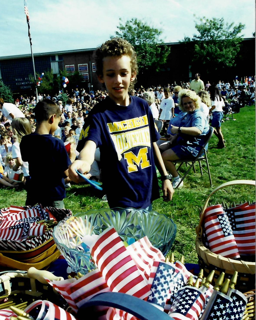 A student puts a piece of paper in a bowl that is surrounded by flags.