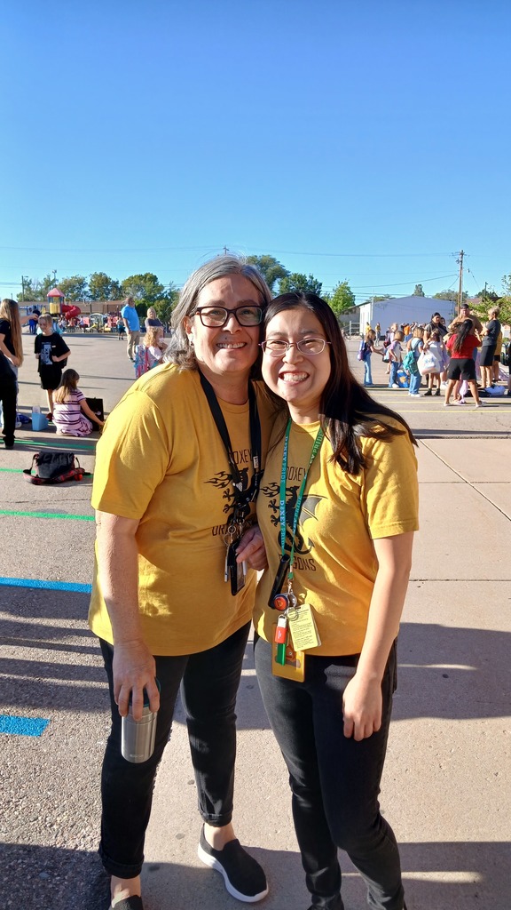 Mrs. Nunez and Mrs. Martinez posing together in their matching yellow doxey dragons shirts waiting for their students.