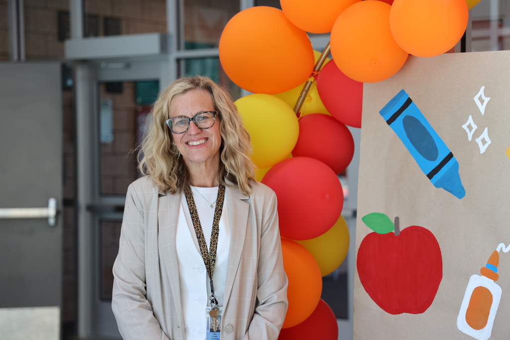 A principal smiles while standing next to a balloon arch.