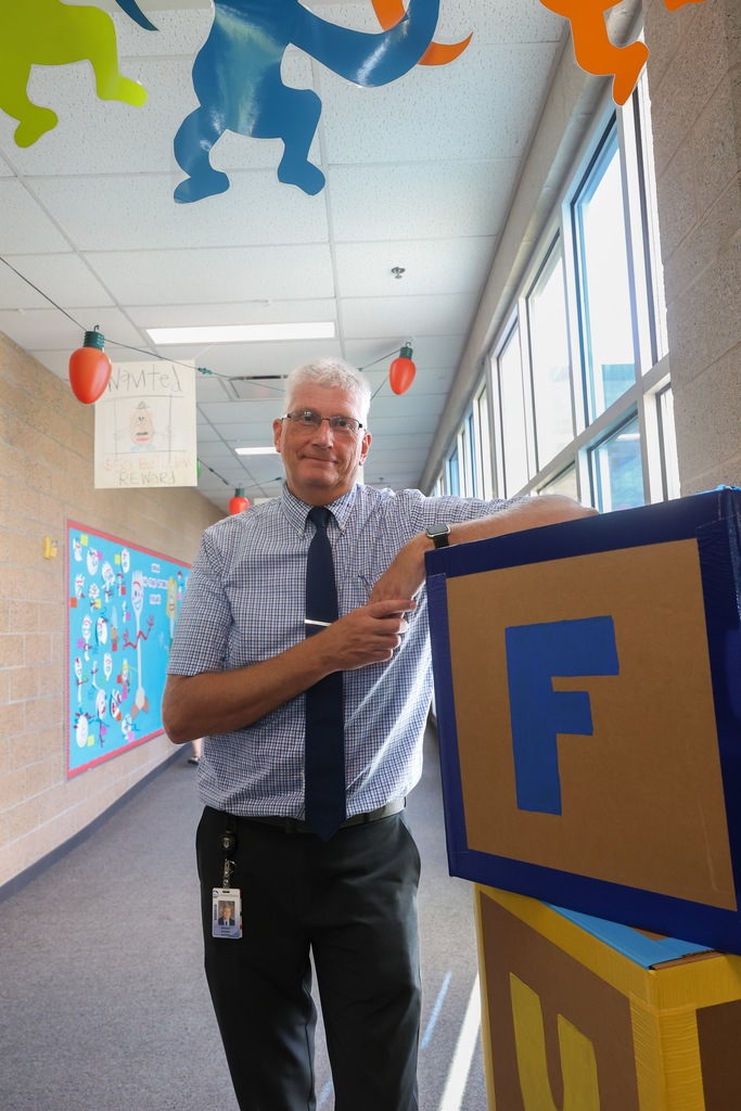 a principal standing against a box that says fun.