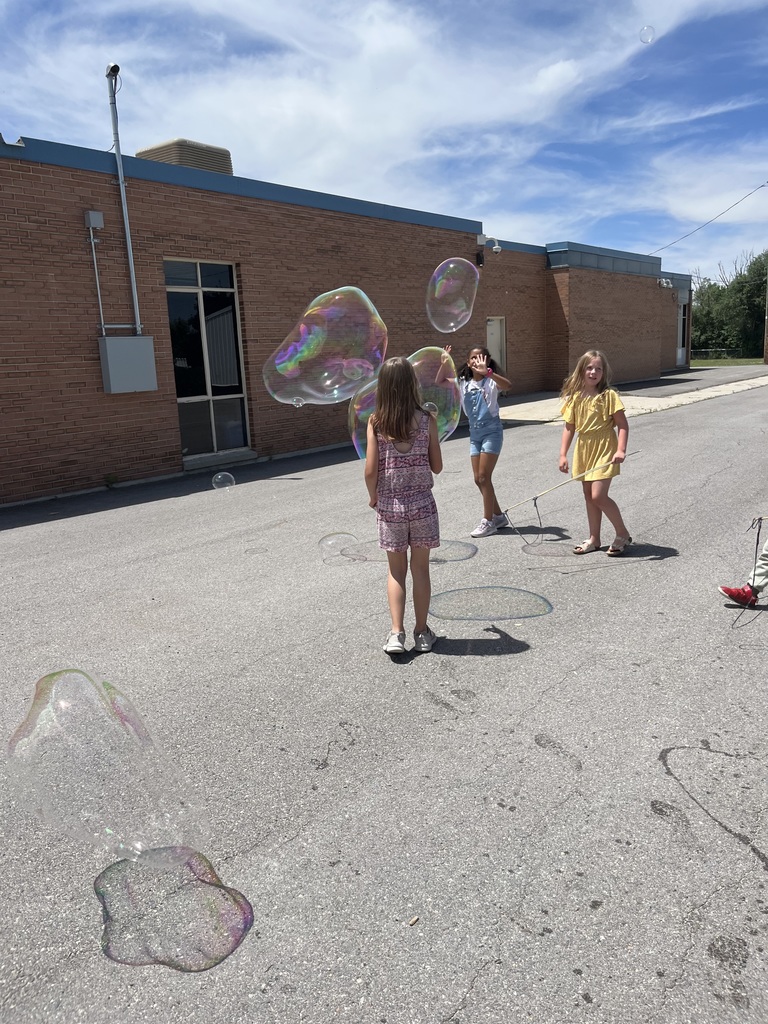 Three girls playing with bubbles out at recess on the blacktop.