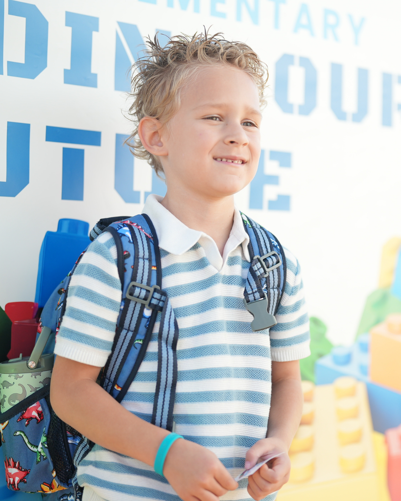 a kindergartener smiling for a photo. He is standing in front of a back drop.