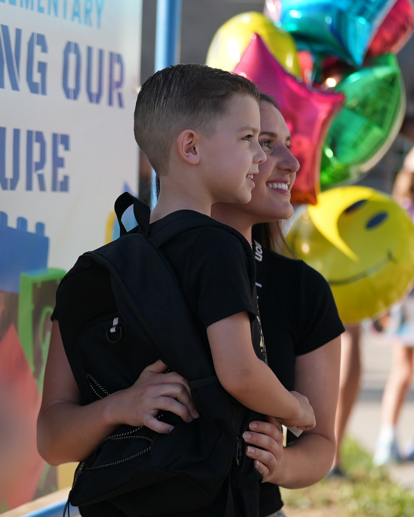 a student and their parent posing in front of a sign and balloons.