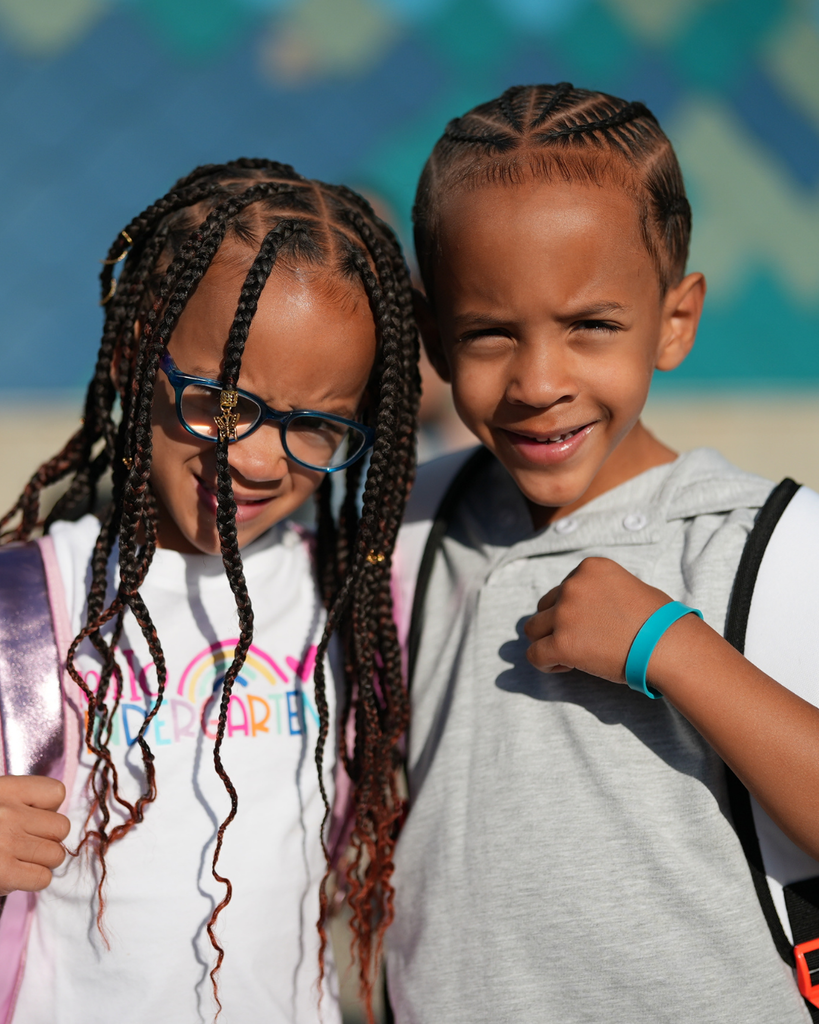 two students smiling at the camera on their first day of kindergarten.
