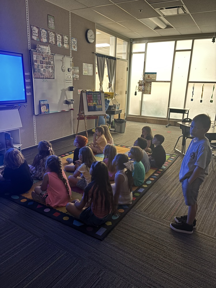 1st graders sitting on a rug looking at images projected on a screen