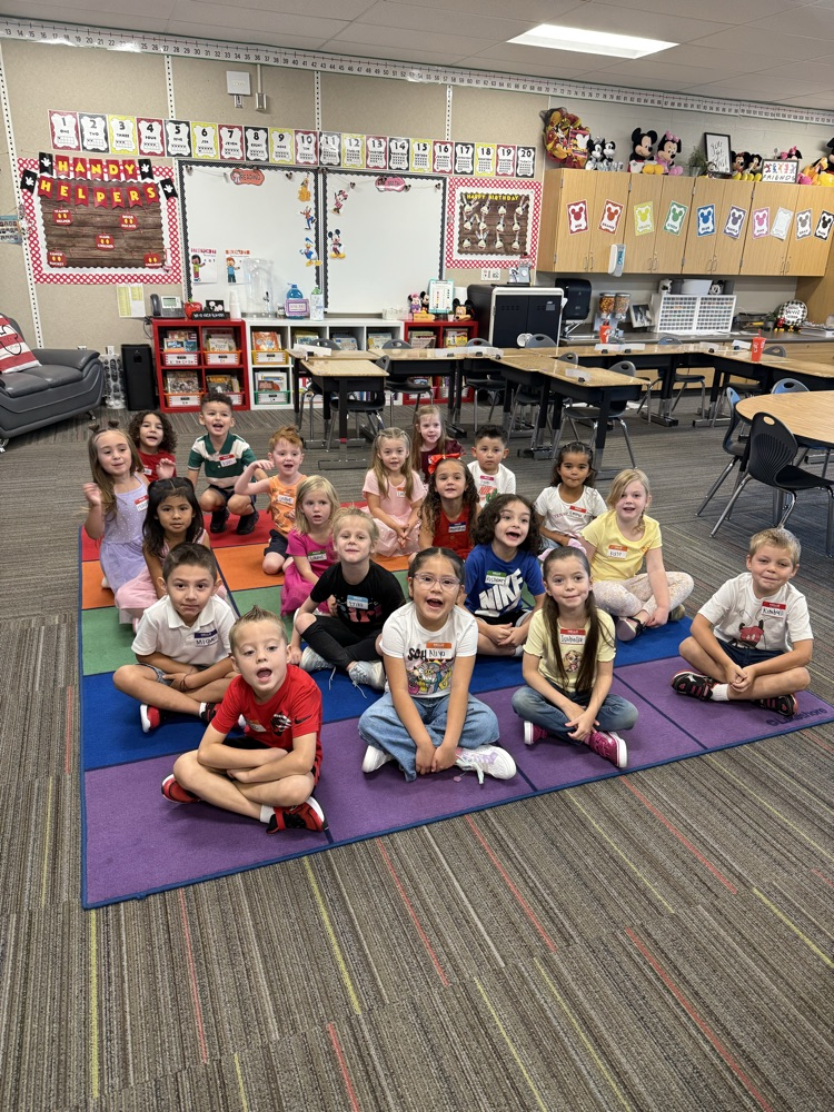 Kindergarteners sitting on a rug smiling al the camera