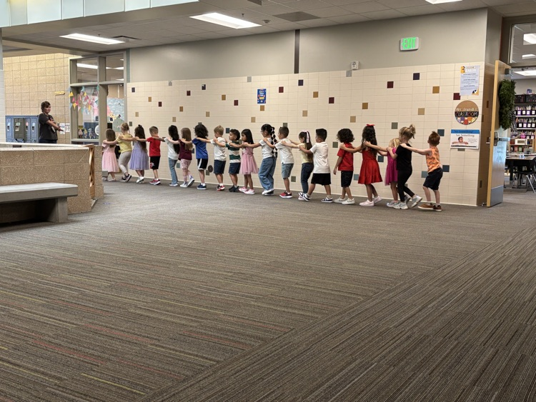 kindergarteners walking in a line with their hands on the shoulders of the person in front of them