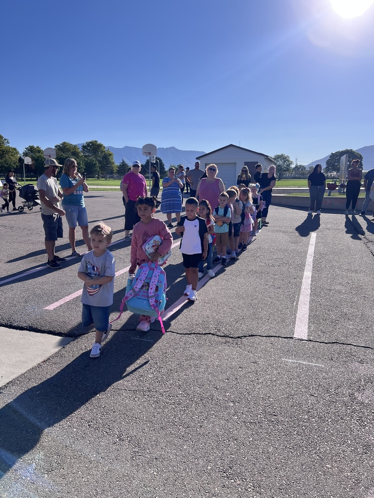 New kindergarten students lining up ready to walk into their classes as parents wait and take pictures off in the background