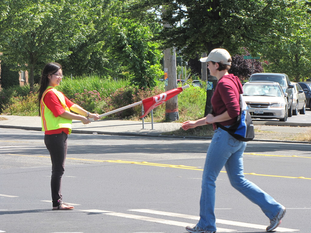 young student crossing street with crossing guard holding flag