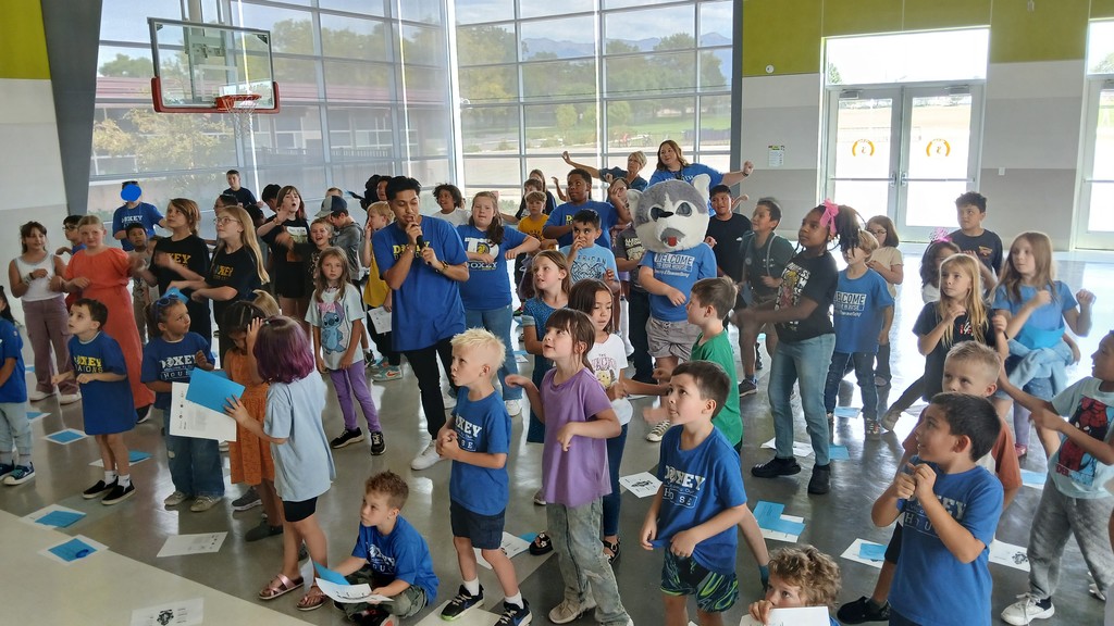 Reveur house wearing blue shirts learning their new song and dance. One student wearing their mascot head, the wolf.