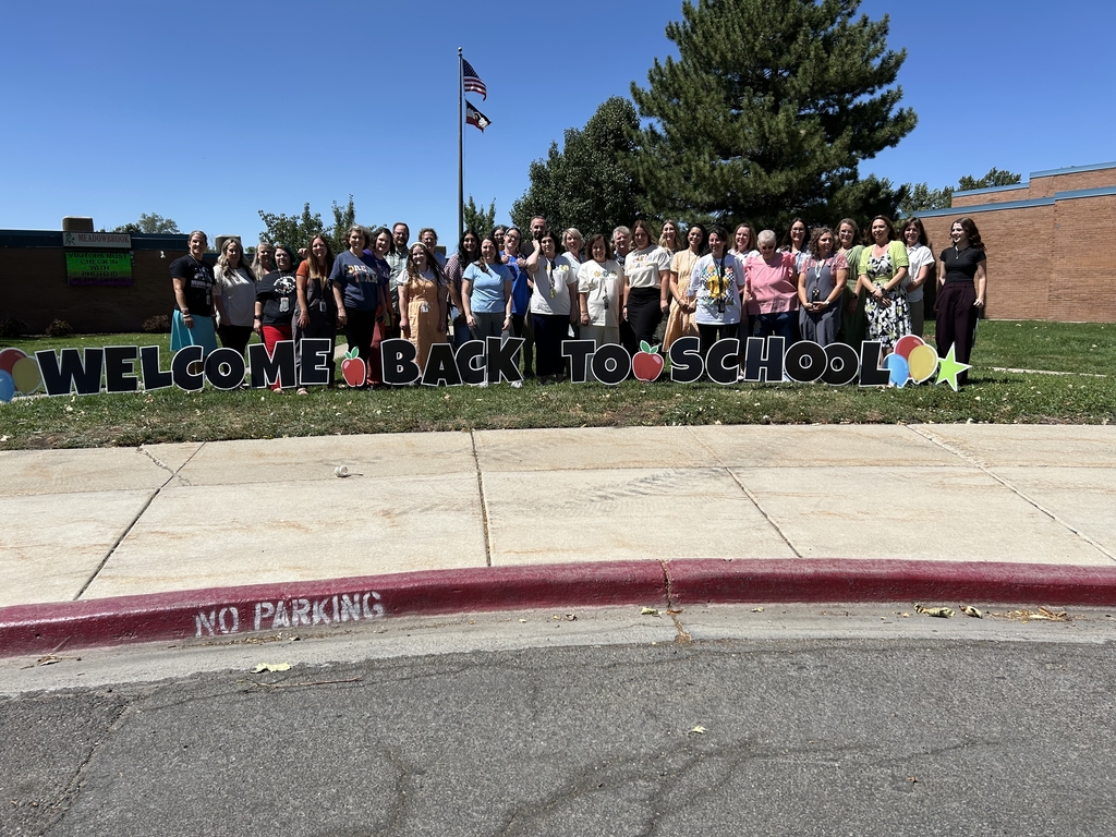 Group of staff standing outside an elementary school on the first day of school, by a sign that says welcome back to school.