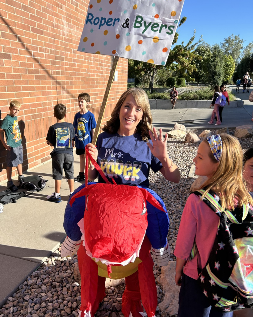 An educator holding a sign that says Roper & Byers is wearing a dragon blow up costume.