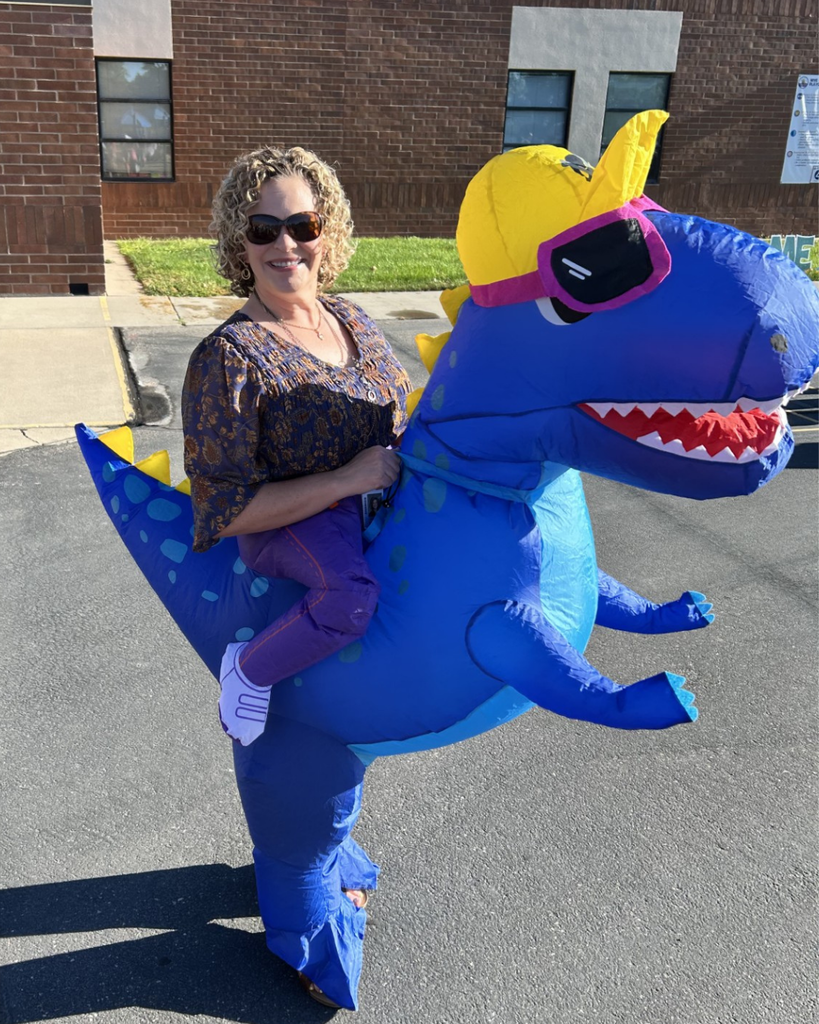 A teacher wearing a blow up blue dinosaur costume.