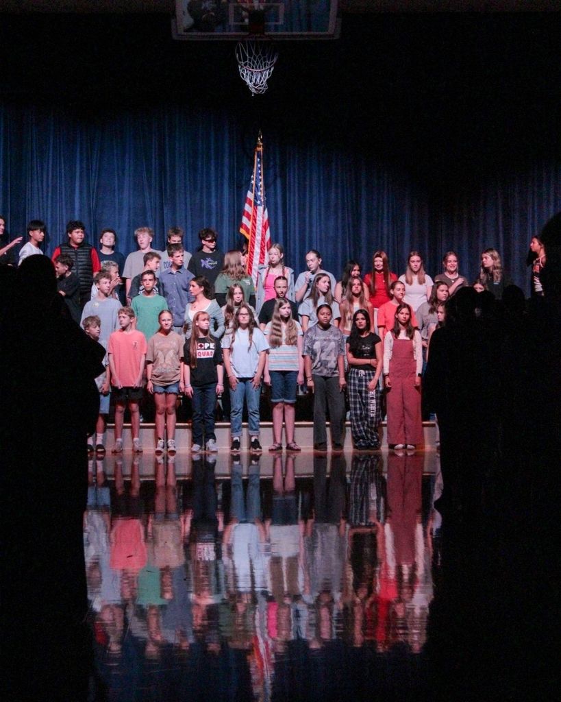 A group of students stand in front of the American flag as they get ready to sing the national anthem for the school assembly. 