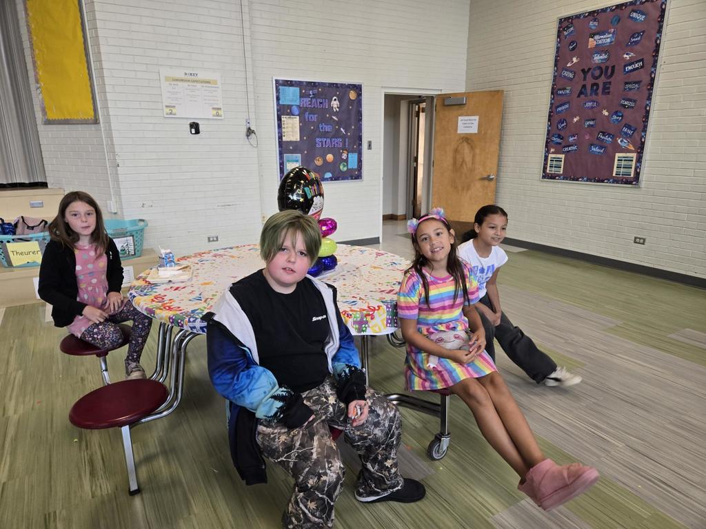 July and August Birthdays kids smiling while sitting at a round table with birthday balloons and a happy birthday table cloth