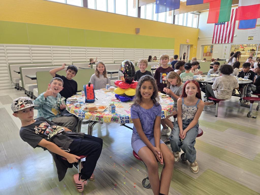 July and August Birthdays kids smiling while sitting at a round table with birthday balloons and a happy birthday table cloth