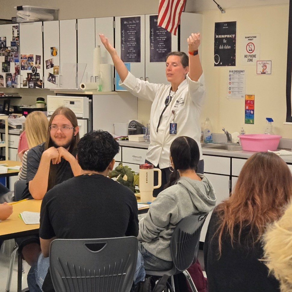Mrs. Nettleship in front of class teaching with arms raised.