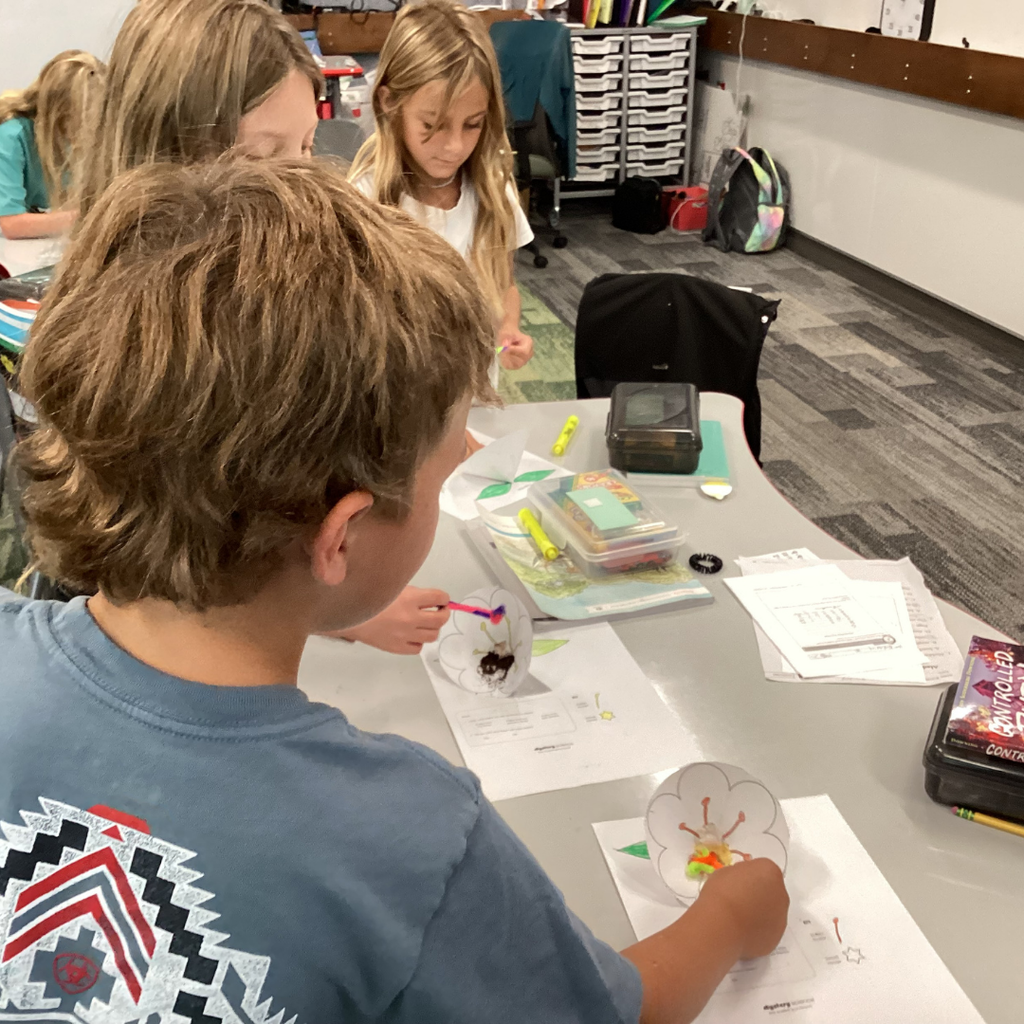 Picture of two girls and a boy student moving pipe cleaners on the inside of a printed flower