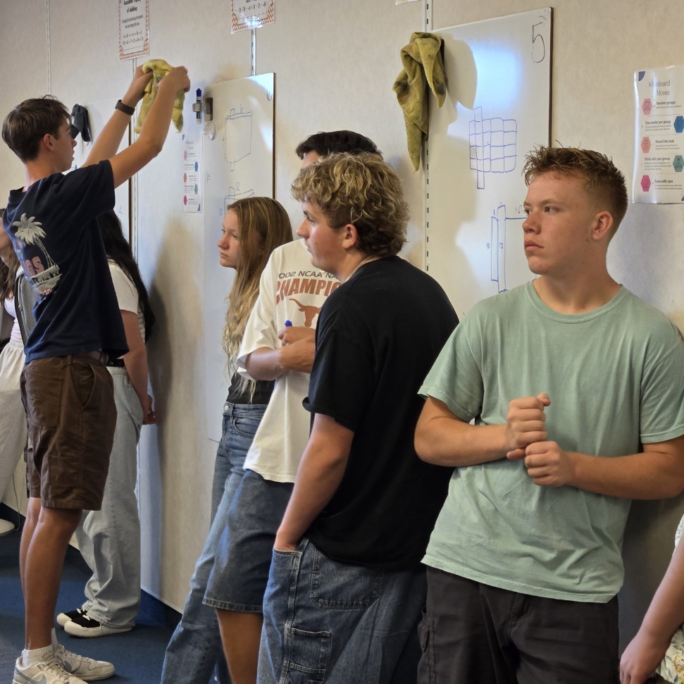 Students in groups at their white boards working on a math problem.