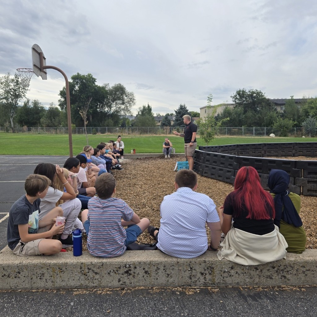 a group of students sitting around a wood chip pit listening to a coach who is teaching them rules. 