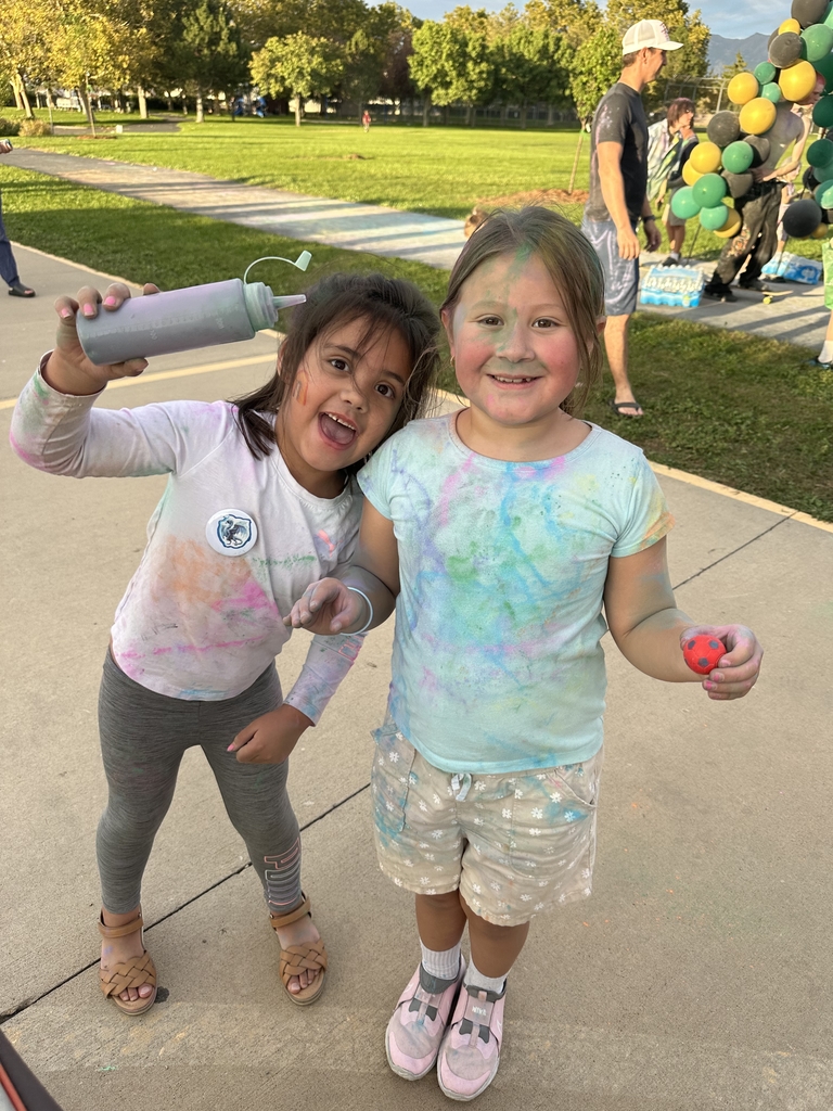 2 students posing with eachother holding a squirt bottle filled with chalk dust while being covered in colorful chalk dust.
