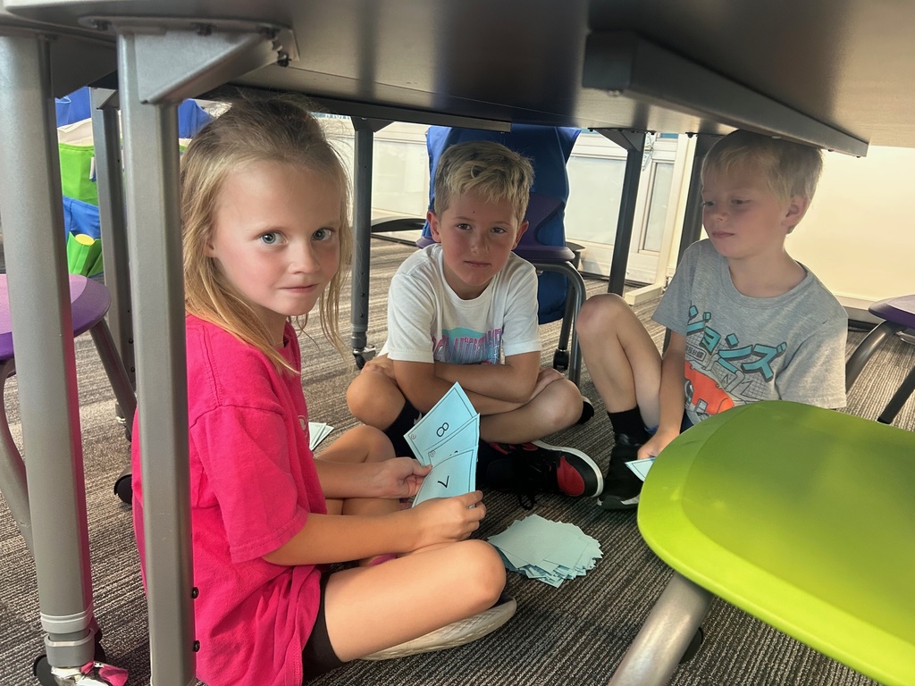 a girl and two boys under desks holding number cards