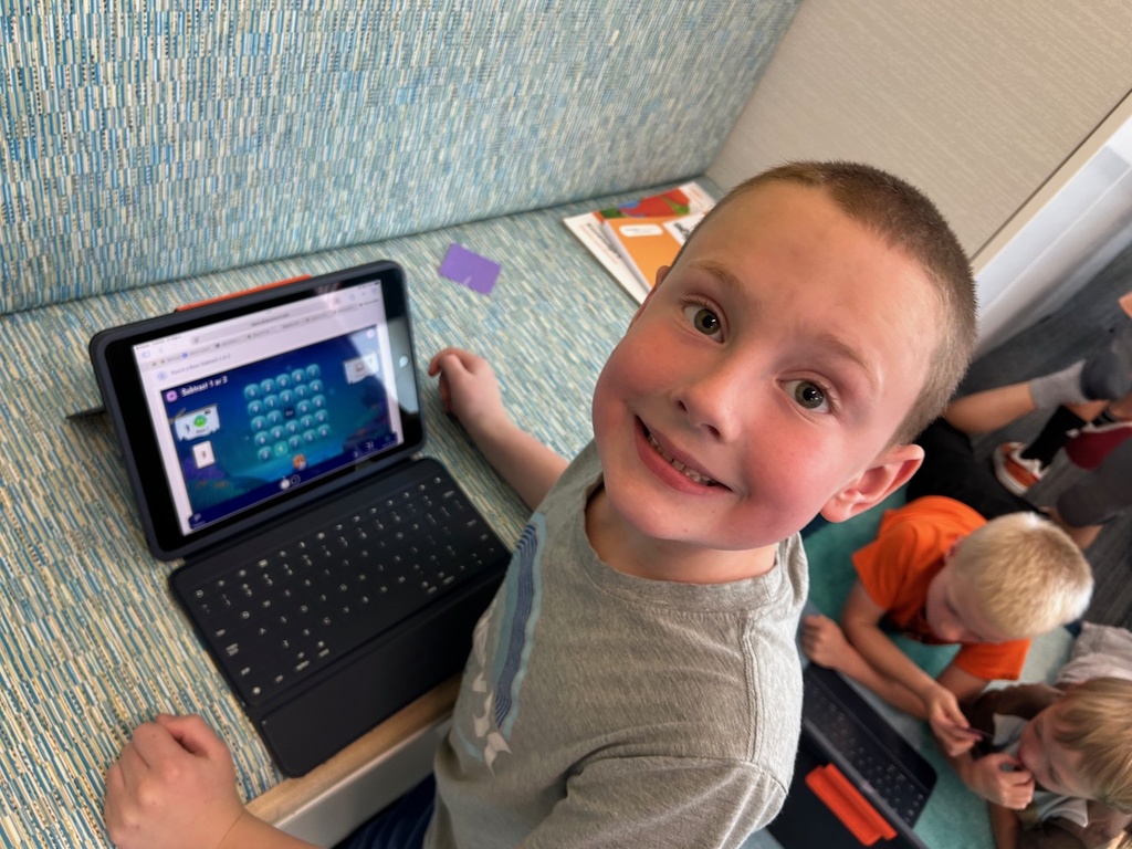 a boy smiling in front of a laptop with a math game on the screen