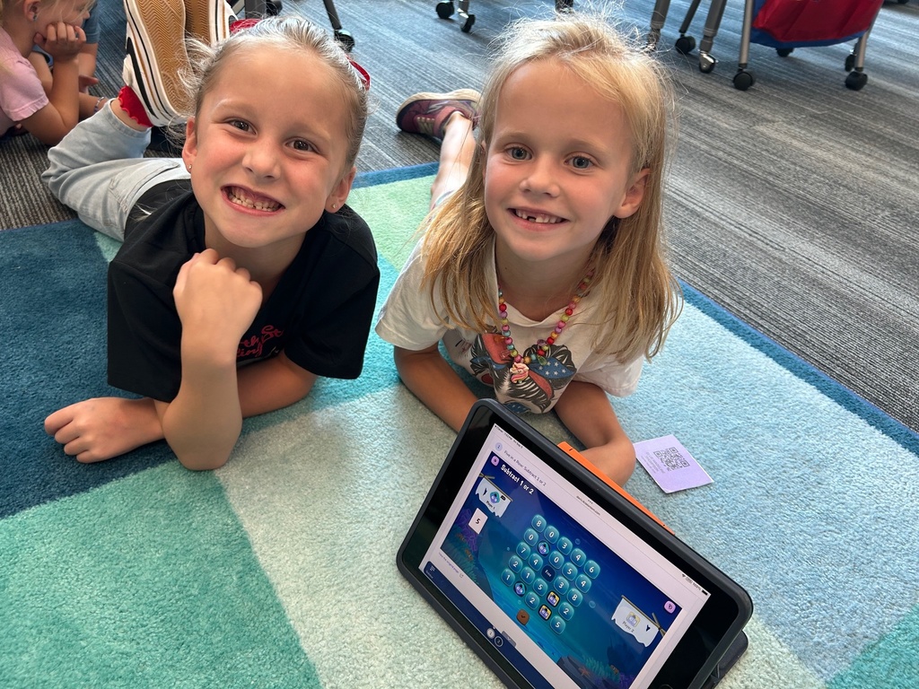 2 girls laying on the ground with an ipad turn to show a math game