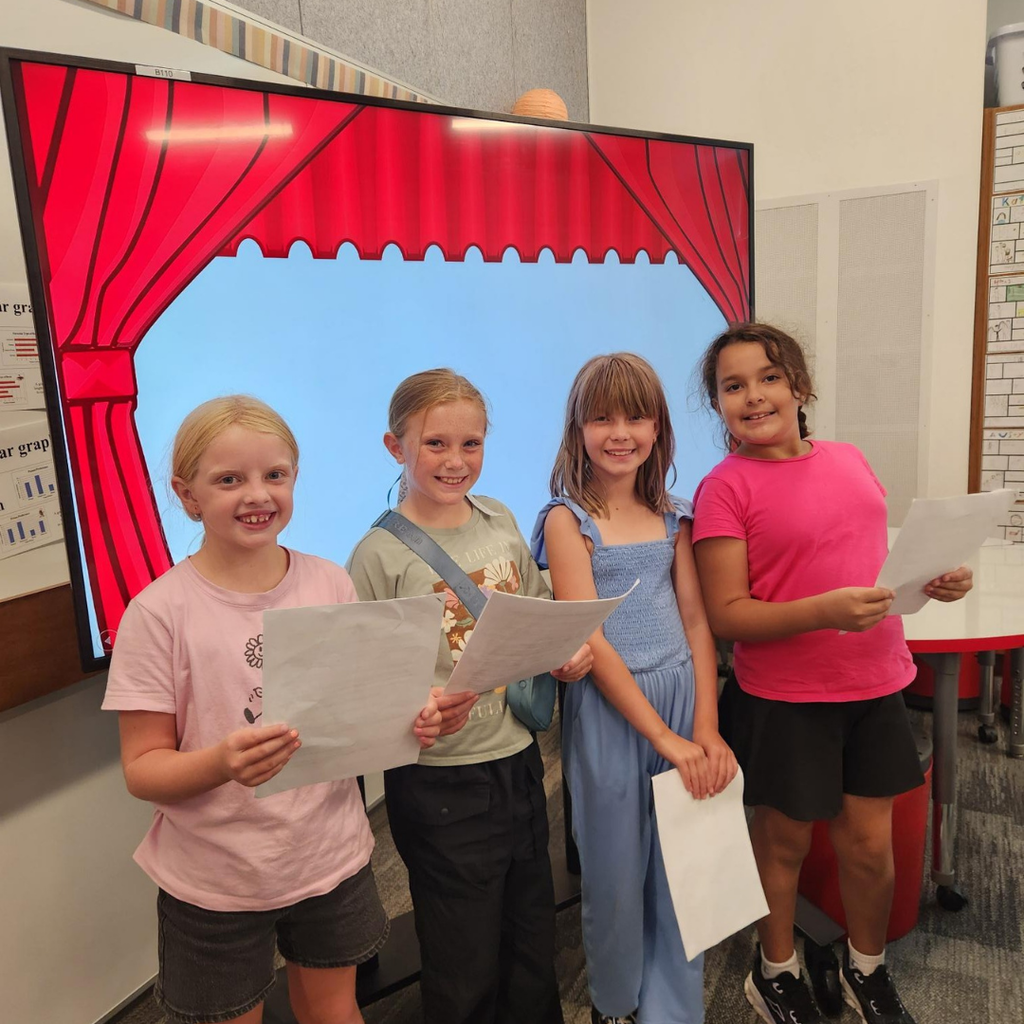 Four smiling girls standing in front of a screen that has curtains on it like the girls are on a stage.