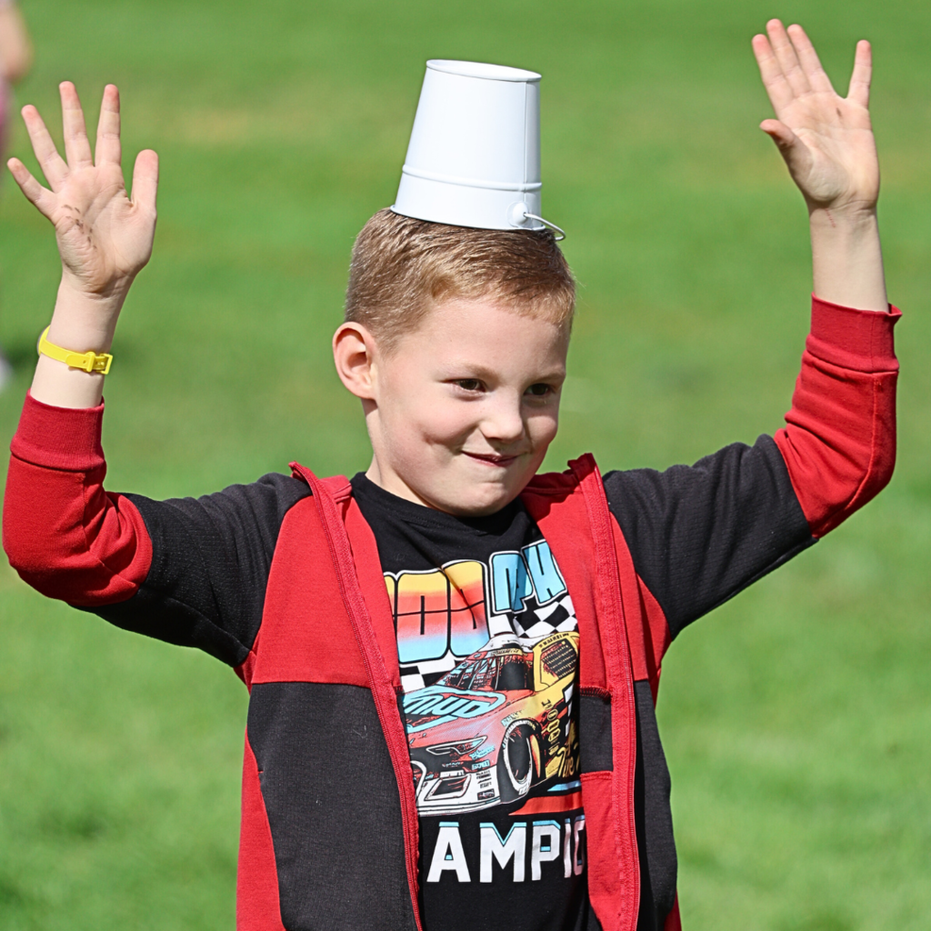 A student with a bucket on his head holds up his arms.