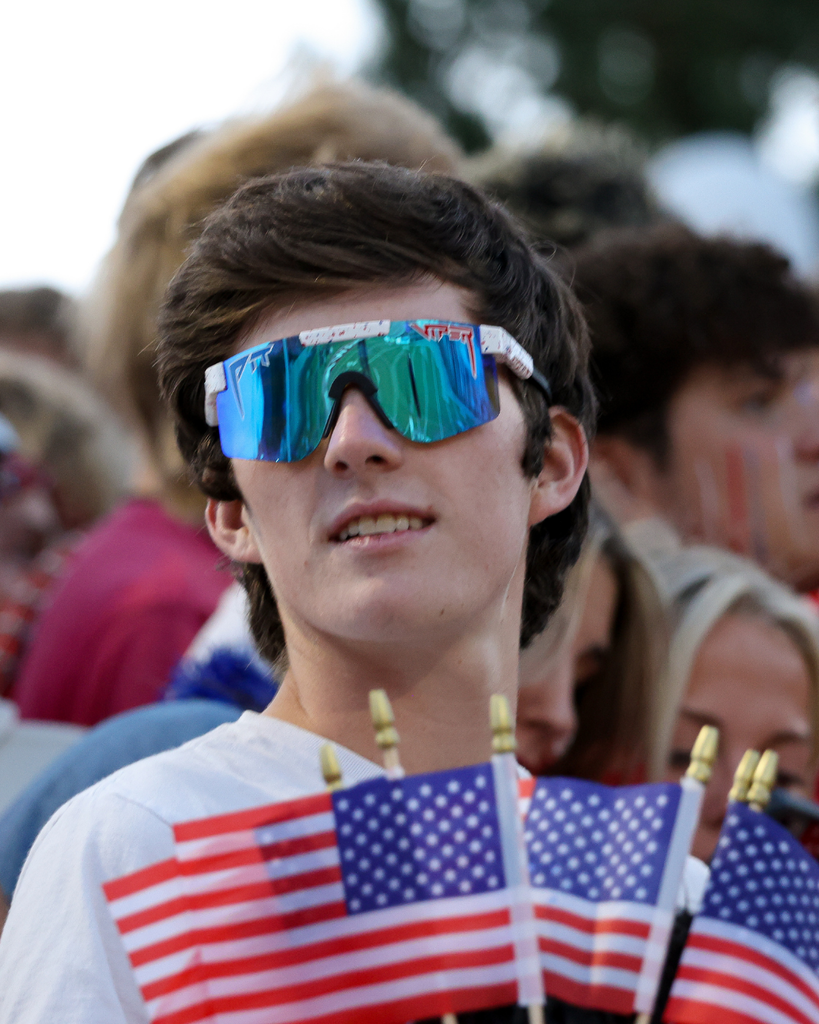 A student wearing blue sunglasses holds a bunch of flags.