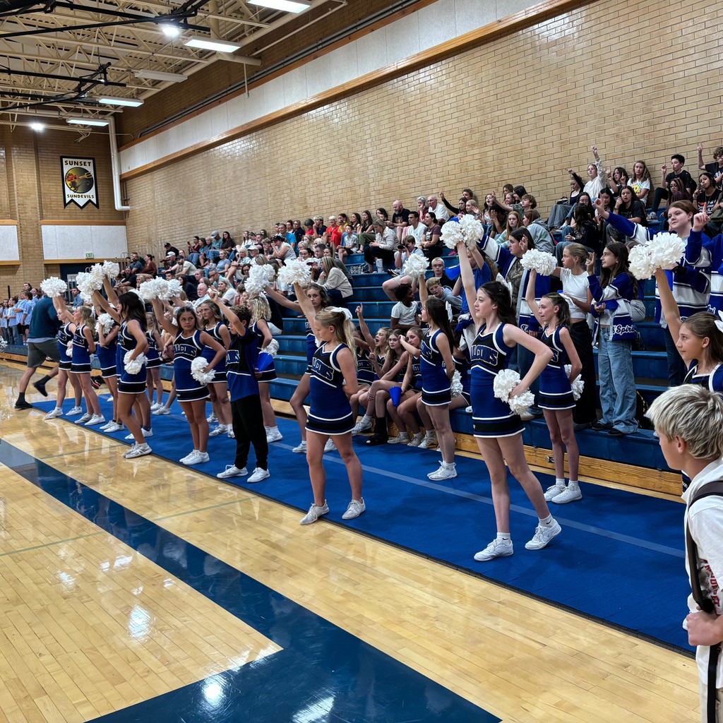 Fairfield's Cheerleaders are standing in the front with crowd members standing on the bleachers in the back.  Everyone is holding up one finger for the one remaining point for Fairfield.