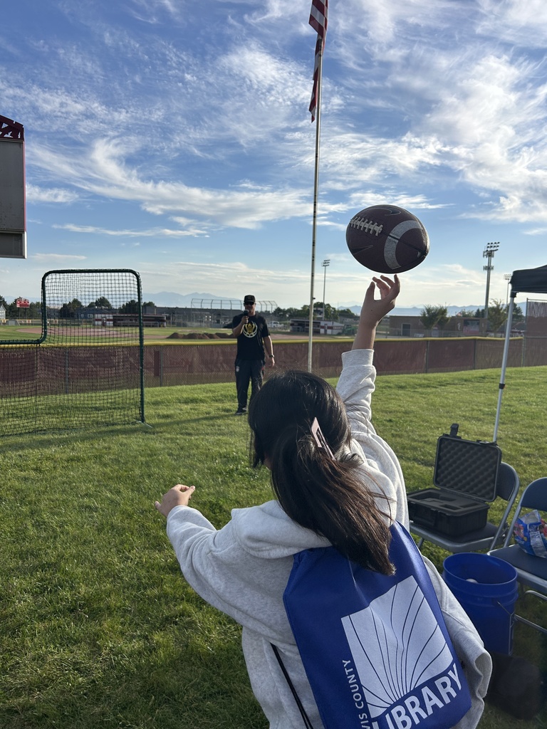 A young girl throws a football as the gym teacher watches.