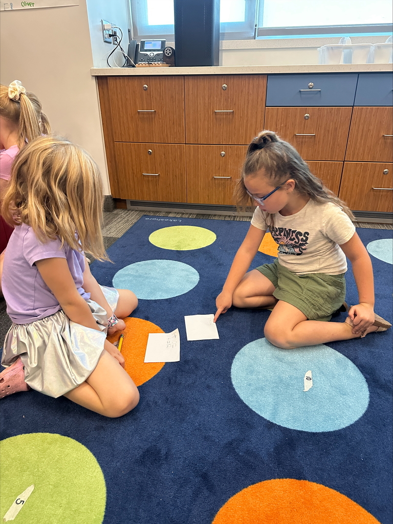 Two students working in a pair on a carpet with paper and pencils