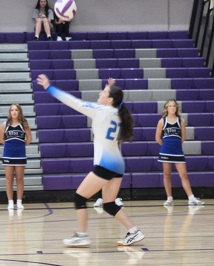 Fairfield's player is serving the ball.  Behind are two cheerleaders standing and watching.