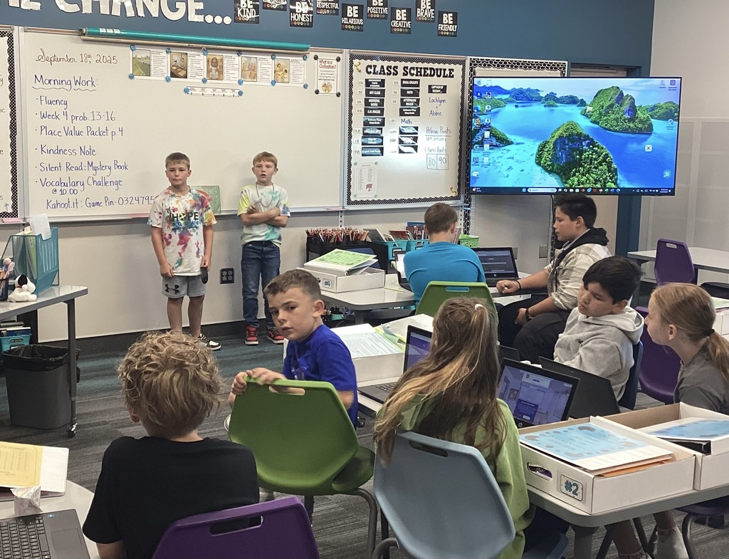 2 boys at the front of a room with group of students in a classroom