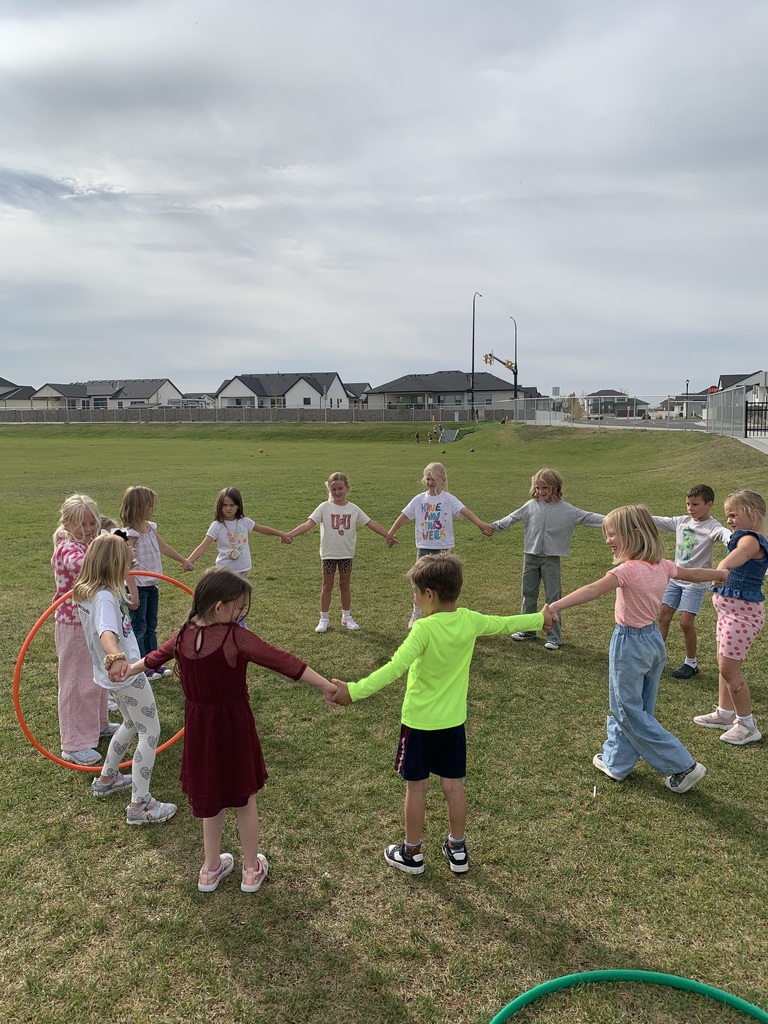 group of students in a field of grass holding hands while moving the hula hoop to the next student